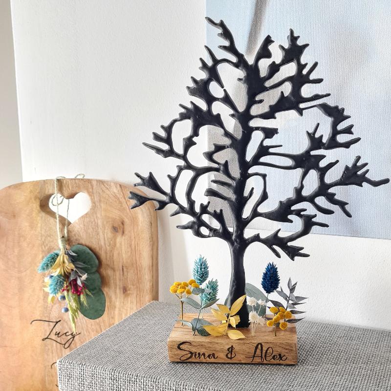 Ein Baum aus Metall mit schönen verzweigten Ästen steht auf einem Holzsockel. Dieser wird nach Wunsch beschriftet und für das Paar individuell mit Trockenblumen gestaltet. Eine ausgefallene Geschenkidee.
