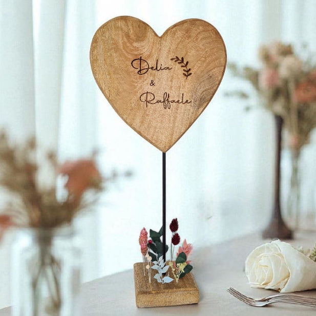 Ein Herz aus Holz steht auf einem Metallständer. Im Holzsockel stecken filigrane Trockenblumen und erinnern an eine romatische Wiese mit Wildblumen. Das Herz kann mit Deinem Wunschtext graviert werden und eignet sich als ganz besonderes Geschenk für Deine Lieblingsmenschen.