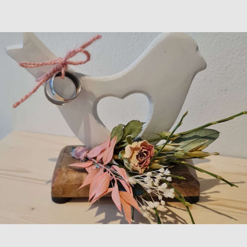 Weiße Aluminiumtaube mit Blumenschmuck in Wunschfarbe auf Holzplatte, Platte ist mit Namen und Datum lasergravierbar.