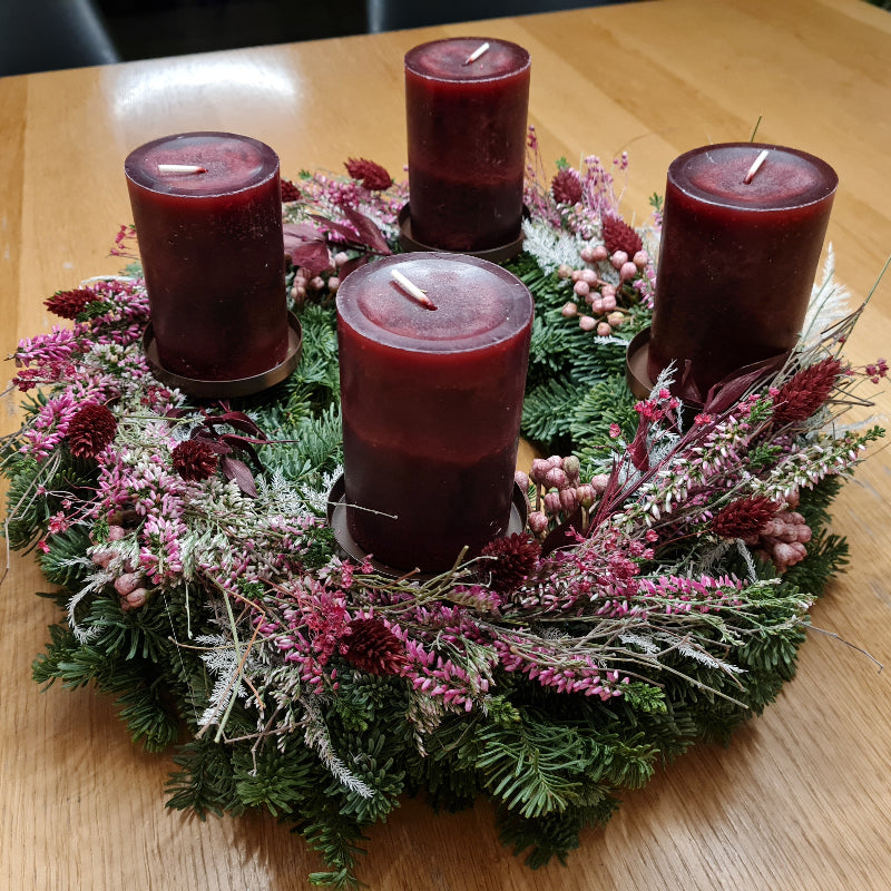 Handgemachter Naturkranz in Beerentönen mit Kerzen. Ein aufgesetzter zweiter Kranz aus Heide und Trockenblumen in weiß und Beerentönen sorgt für ein neues Erscheinungsbild im ansonsten klassischen Adventskranz.