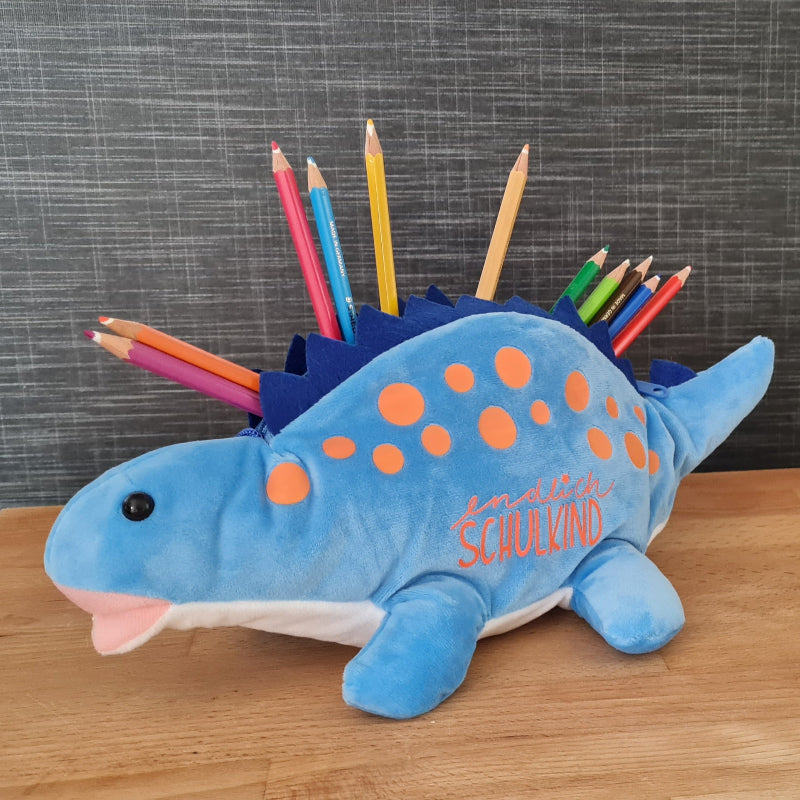 Personalisierbares Mäppchen zur Einschulung mit Name – Geschenk zur Schultüte. Ein kuschliger blauer Dino mit orangenen Punkten zur Stifteaufbewahrung. Er trägt den Schriftzug "endlich Schulkind" und ist ein ideales Geschenk zur Einschulung.