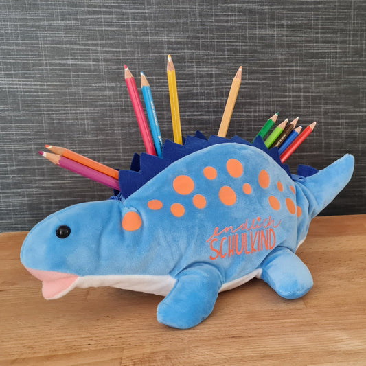 Personalisierbares Mäppchen zur Einschulung mit Name – Geschenk zur Schultüte. Ein kuschliger blauer Dino mit orangenen Punkten zur Stifteaufbewahrung. Er trägt den Schriftzug "endlich Schulkind" und ist ein ideales Geschenk zur Einschulung.