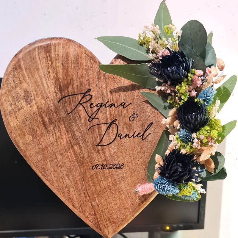 Ein ganz besonderes und ausgefallenes Geschenk zur Hochzeit. Ein Herz aus Holz auf Metallfuß zur Hochzeit. Das Geschenk ist personalisiert und liebevoll mit Blumen geschmückt.. Der Name des Brautpaars und das Datum sind in das Holzherz graviert. Saisonale Trockenblumen dekorieren das Herz.