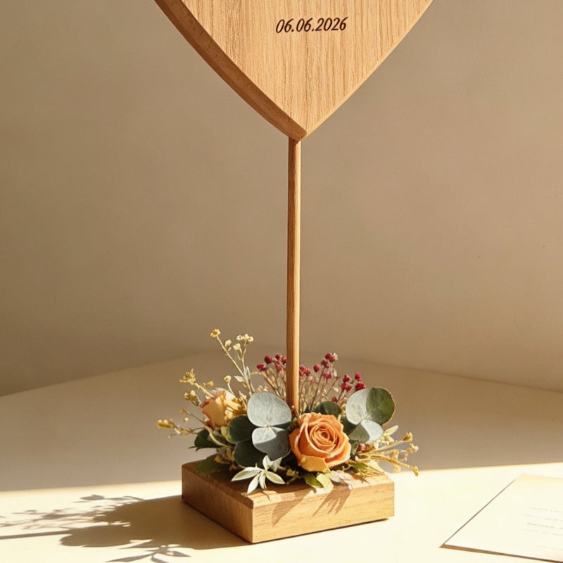 Ein Herz aus Holz steht auf einem Holzsockel, welcher mit Trockenblumen dekoriert an eine romantische Wiese mit Wildblumen erinnert. Das Herz ist graviert werden und eignet sich als ganz besonderes Geschenk zur Hochzeit.