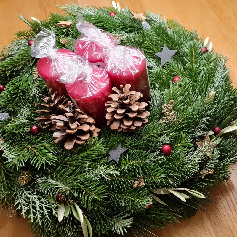 Natürlicher Adventkranz aus frischem Tannengrün und Stumpenkerzen in Rot, geschmückt mit Holzdeko, Zapfen, Thuja und Pistazie