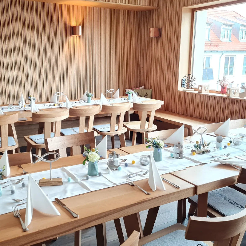 Eine bunte Tischdekoration mit fröhlich gefüllten Vasen, bunten Filzbommeln und Fischen in einem sehr modernen Restaurant in Holzbauweise.