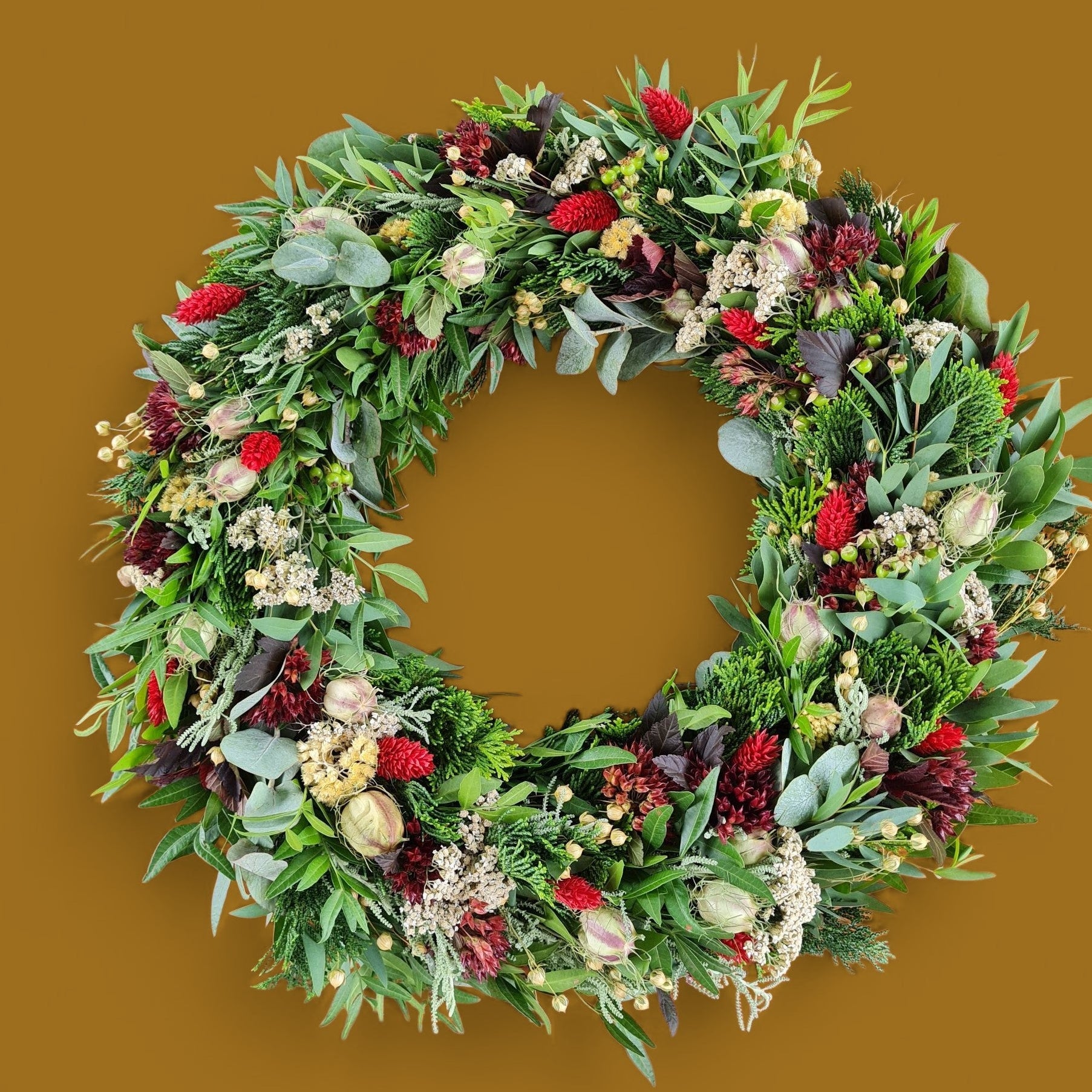 Moderner Tür und Wandkranz aus Naturmaterialien und Trockenblumen in den klassischen Farben grün und rot