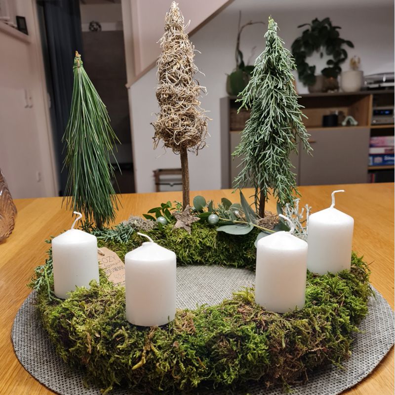 Adventskranz nach Wunsch auf Mooskranz, dekoriert mit drei Dekobaeumen, Eukalyptus, Holzdeko und vier Stumpenkerzen.