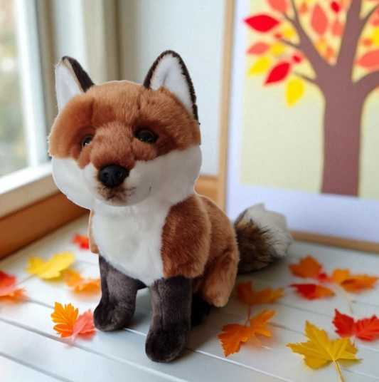 Ein flauschiger, naturgetreu gearbeiteter Fuchs aus Plüsch sitzt zwischen bunten herbstblättern. Die Zeit des Schulbeginns ist auch die Zeit der waldtiere. der Fuchs ist ein besonderes Geschenk für Kinder und gibt kuschligen Halt in der Schulzeit.