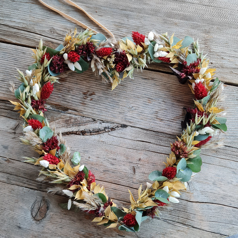 Ein bezauberndes Herz aus sommerlichen Blüten und Gräsern gebunden. Es dekoriert eine Hochzeitfeier und kommt an den Stuhl der Braut.
