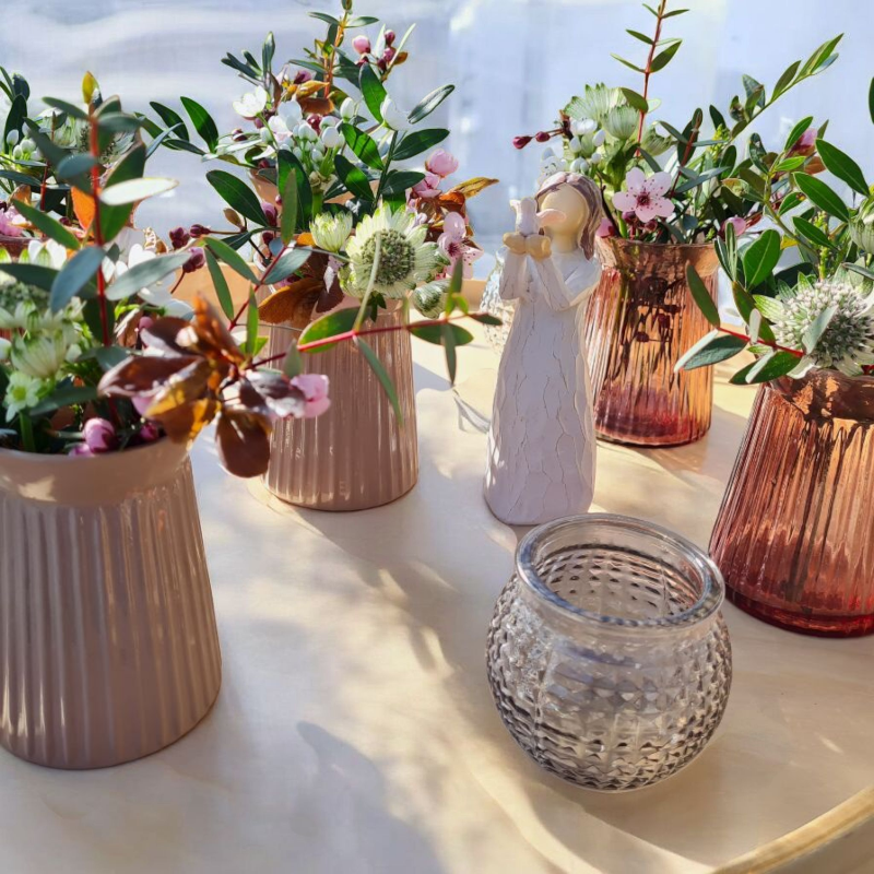 Unsere beliebten Vasen in nude und nougat Farben, gefüllt mit zarten Blüten und Blättern zur Dekoration einer Kommunionfeier. Ein Engel mit Taube ist das zentrale Motiv dieser modernen Tischdekoration.