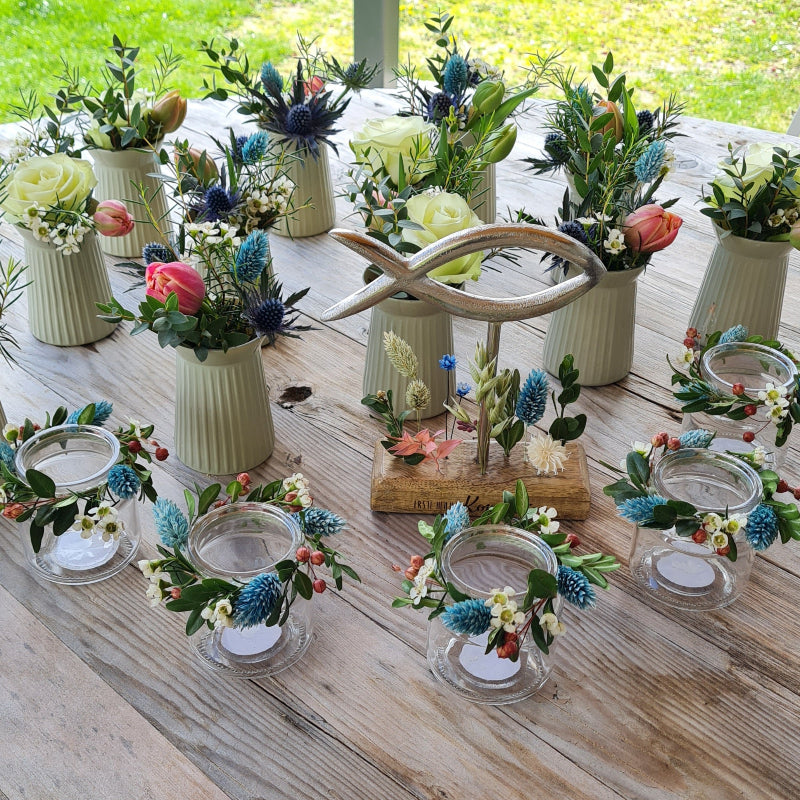 Tischdekoration mit Vasen und Windlichtern. Die Vasen sind bunt gefüllt und die Windlichter tragen passende Kränze aus zarten Trockenblumen und Buchs. Klassisch ganz modern interpretiert.
