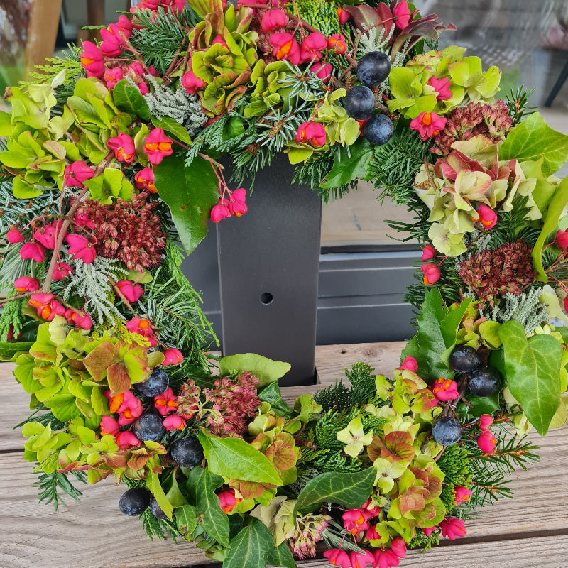 Bunter Tischkranz als Dekoration für ein Familienfest im Herbst. Der Kranz trägt Beeren und Früchte, Hortensien und Efeu.