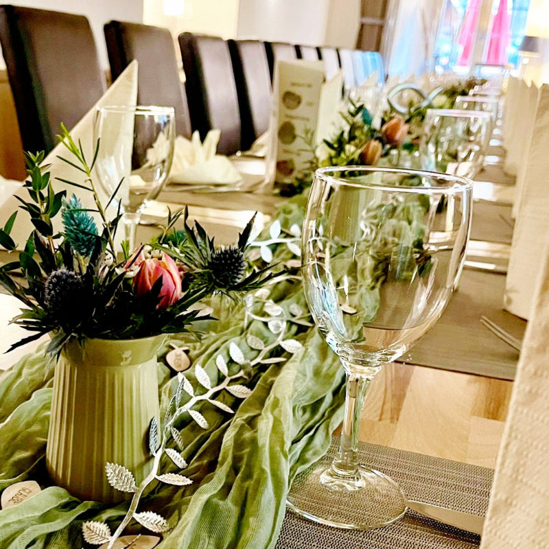 Eine festlich dekorierte Tafel zu einer Kommunionfeier. Die Tischdekoration besteht aus grünen asen, Tischbändern, zarten Ranken und bunten Blumen.