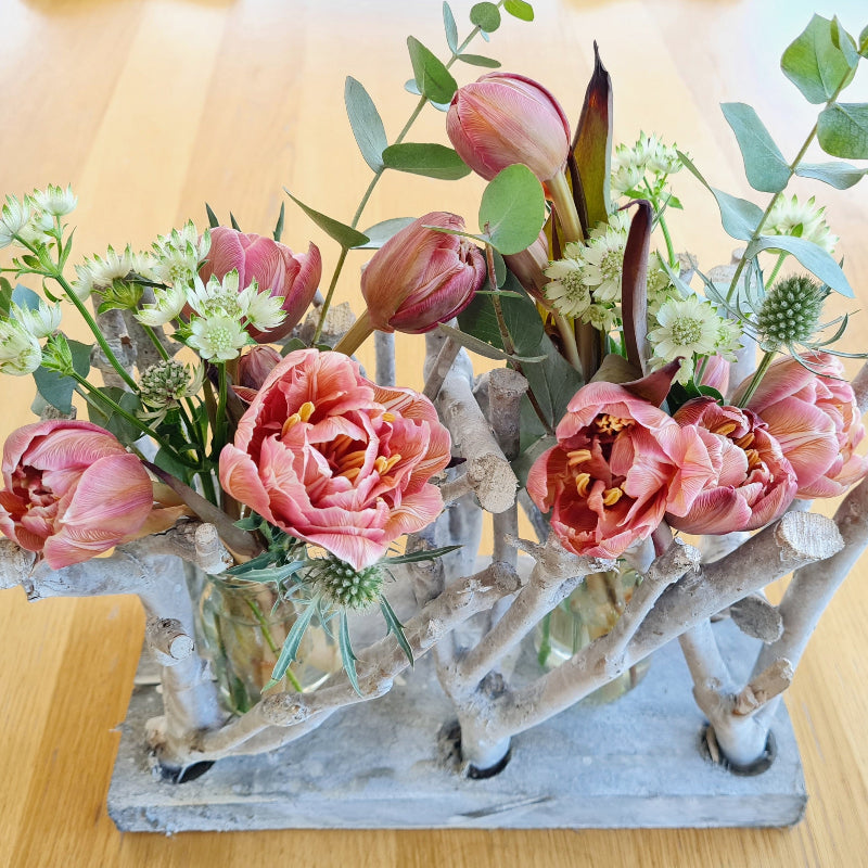 Eine sehr moderne Tischdekoration mit Eukalyptus und sehr speziellen gefärbten Tulpen, kombiniert mit Distel und zarten Sterndolden. Die Floristik steht in einem Arrangement aus gekalkten Zweigen.