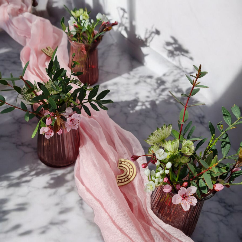 Zarte Blüten in modernen Vasen in Beerenfarben, ergänzt mit passendem Tischband in rosa und kleinen Regenbögen aus Holz. moderne Tischdekoration zu Kommunion, Taufe oder Konfirmation.