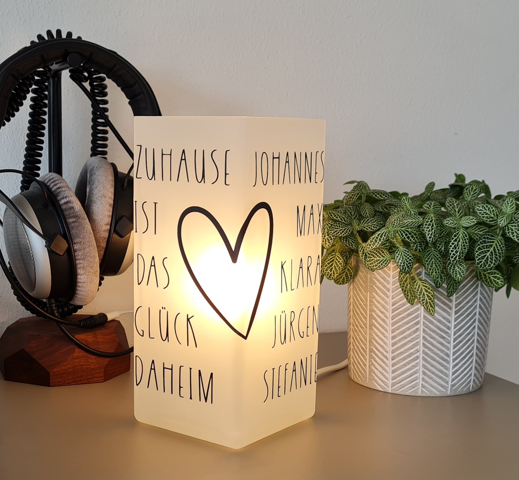 Eine personalisierte Lampe mit Spruch Zuhause ist das Glück daheim. Daneben finden die Namen aller Familienmitglieder Platz. Verziert mit einem Herz im Handlettering Stil ist diese hübsche Tischleuchte ein originelles Geschenk zum Einzug in ein neues Zuhause. Modern, elegant und schlicht gehalten.